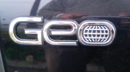 Эмблема автомобильной марки GEO. Определить какие типы АКПП установлены в моделях автомобилей GEO.
